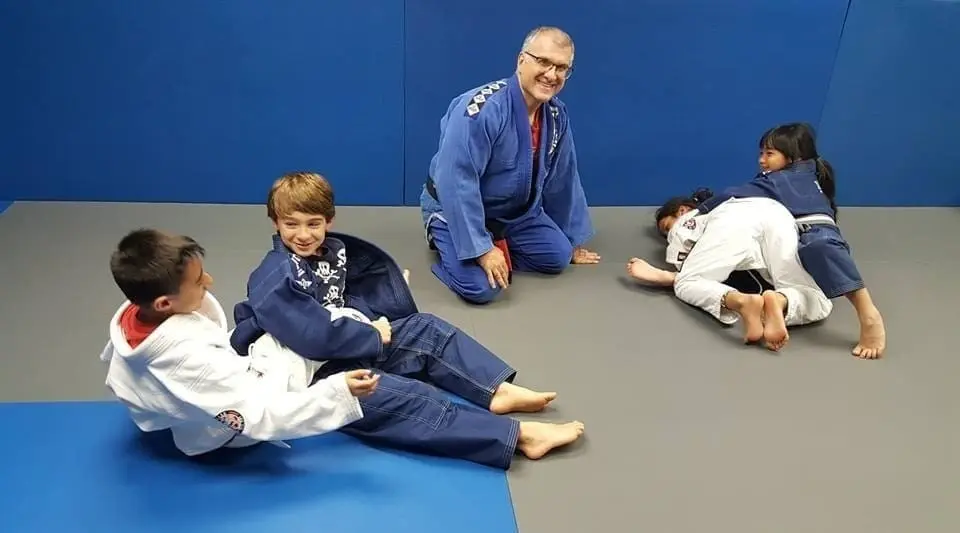 Brazilian Jiu-Jitsu instructor coaching children during kids grappling class on training mats.